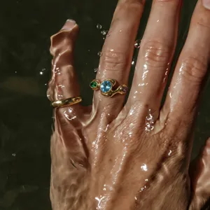 Macro shot of 18K gold plated wavy rings with vibrant gemstones in rippling water