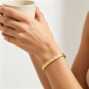 Close-up van een gouden geometrische piramidearmband gedragen om de pols met een witte mok.