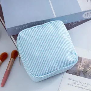 Primer plano detallado de un neceser de maquillaje seersucker a rayas azul claro en mesa.