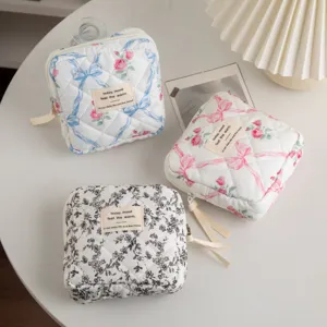 Detail view of three quilted floral cosmetic bags with ribbon patterns on a white table