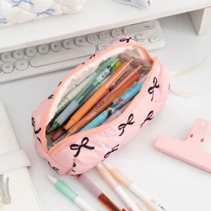Close-up detail of a pink quilted pencil case with black bow patterns filled with pens