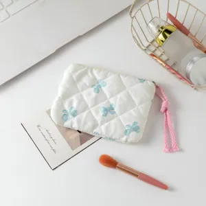 Detalle de un neceser acolchado con lazos azules y una borla rosa en un escritorio blanco