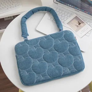 Detail einer blauen Denim-Laptoptasche mit weißem Apfelmuster und weichem Griff.