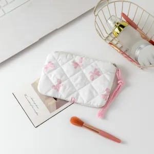 Neceser acolchado blanco con estampados de lazos rosas y brochas de maquillaje