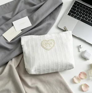 Close-up of white lace makeup bag with heart bow detail and striped fabric texture.