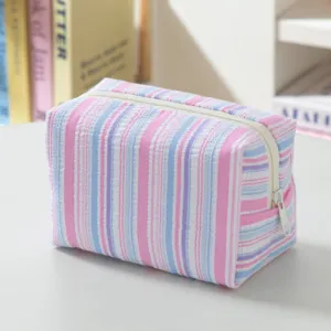 Detailed close-up of the striped seersucker makeup bag showing soft texture and zipper.