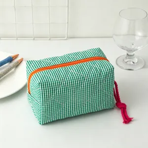 Detalle de una bolsa de cosméticos a cuadros verdes con cremallera y borla
