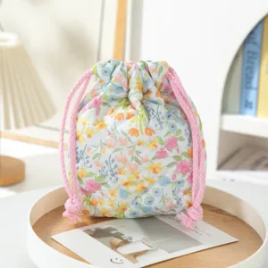 Detail view of a quilted floral drawstring makeup pouch with pink twisted rope ties on a tray