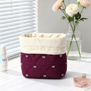 Detail view of a quilted burgundy drawstring makeup bag with white bow embroidery