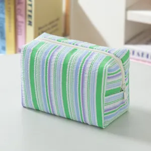 Detail view of a fresh striped seersucker cosmetic bag with textured green and blue stripes