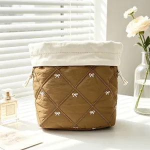Detail of a brown quilted drawstring makeup bag with white bow embroidery on a desk.