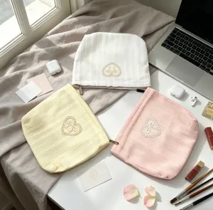 Soft fabric cosmetic bags with bow embroidery in pink, white, and yellow colors.