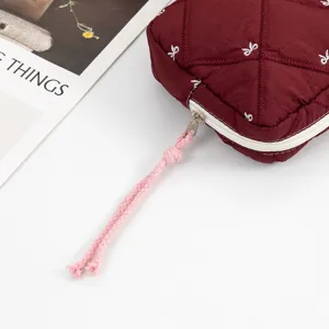 Close-up detail of burgundy quilted cosmetic bag featuring white bow embroidery and pink rope