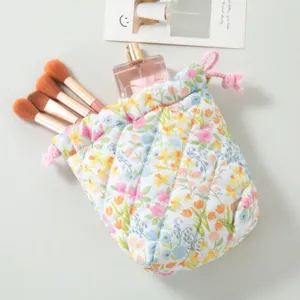 Close-up of quilted floral cosmetic bag with drawstring closure and makeup brushes inside.