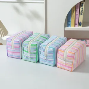 A group of four colorful striped seersucker cosmetic bags displayed on a white desk