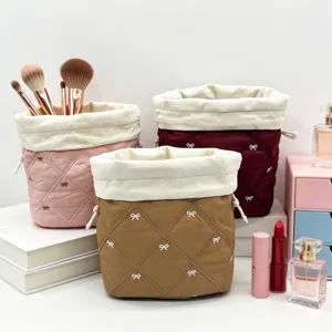 Group of three quilted drawstring makeup bags with bow embroidery in a vanity setting