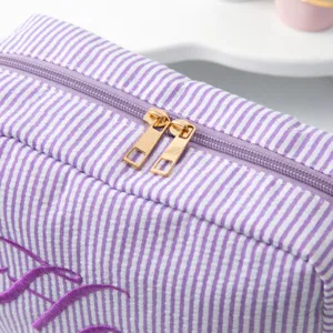 Gros plan d'une trousse de maquillage rayée avec fermeture éclair dorée et broderie