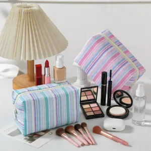 Striped seersucker makeup pouches arranged with various beauty products on white table