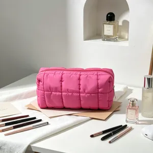 Neceser acolchado rosa de estilo puffer con pinceles de maquillaje y botes de perfume.