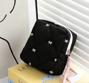 Detailed close-up of a quilted black cosmetic bag featuring white embroidered bow patterns
