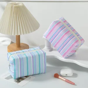 Detailed close-up showing the striped seersucker texture of two pastel travel makeup bags
