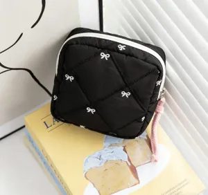 Close-up detail of black quilted cosmetic pouch featuring white bows and pink puller