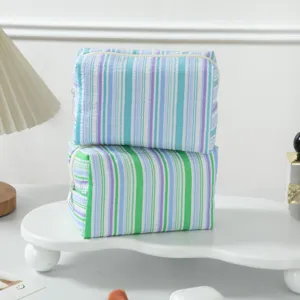 Detailed view of stacked striped seersucker cosmetic bags in blue and green colors