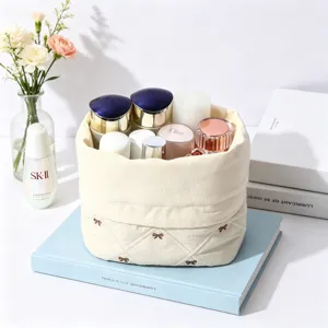 Detail view of a soft quilted cream cotton cosmetic bag featuring delicate brown bow embroidery.