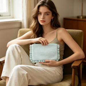 Seersucker striped makeup bag with ruffle trim held by a model in a cozy setting.