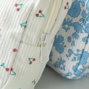 Dettaglio ravvicinato della pochette in velluto a coste con stampa floreale e zip bianca.