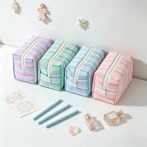 Group of four striped seersucker cosmetic bags in soft pastel colors on a white table