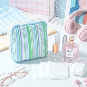 Detail of a portable striped seersucker cosmetic pouch with lifestyle props background