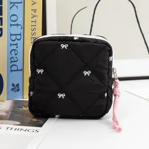 Close-up of black quilted pouch with white bow patterns on a white table with books.