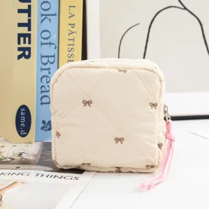 Close-up of cream quilted toiletry bag featuring embroidered bows and a pink zipper pull