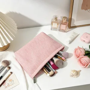 Gros plan d'une trousse à maquillage en seersucker à rayures roses sur coiffeuse blanche