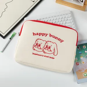 Détail d'une housse d'ordinateur crème avec broderie lapin rouge dans un bureau