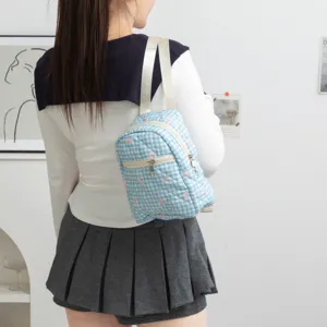 Vista trasera de mochila acolchada a cuadros azules con bordado de lazo rosa en modelo