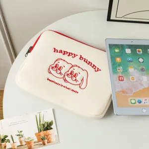 Détail d'une housse d'ordinateur brodée petit lapin à côté d'une tablette iPad