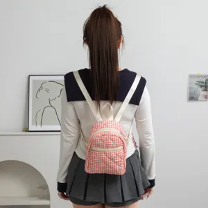 Vista trasera de modelo con mini mochila acolchada a cuadros rojos y lazos bordados.