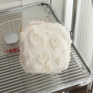 Detail van een crème pluche make-uptas met hartjespatroon op een metalen rek.