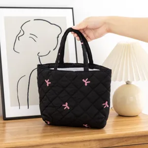 Neceser de maquillaje acolchado negro con bordado de mariposa rosa sostenido a mano