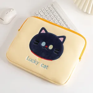 Detail van gele laptophuls met geborduurde zwarte kat en Lucky cat tekst op bureau.