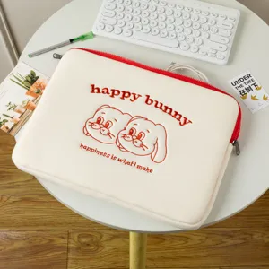 Gros plan détaillé de la jolie broderie "happy bunny" sur une housse d'ordinateur crème douce.