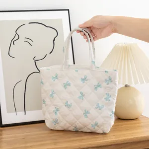 Vista detallada de bolsa acolchada blanca con estampados de lazos azul claro y asas suaves
