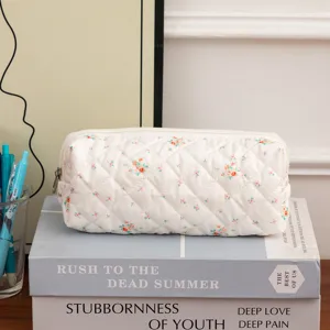 Close-up of a white quilted cotton pouch with delicate floral patterns on books.