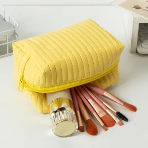 Detail van gele gewatteerde PU make-up tas met penselen en flesje