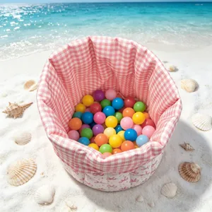 Close-up of pink bowknot quilted fabric storage basket filled with colorful balls on beach.