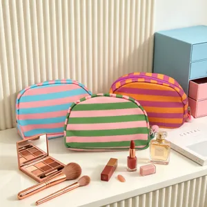 Close-up of three colorful striped cosmetic bags with makeup accessories on a white desk.