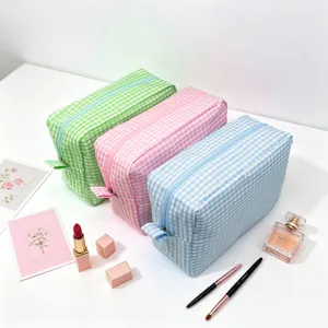 Set of three pastel seersucker plaid makeup bags with zip closure on white table.