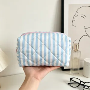 Detail of a hand holding a blue and white striped quilted makeup bag with pink zipper